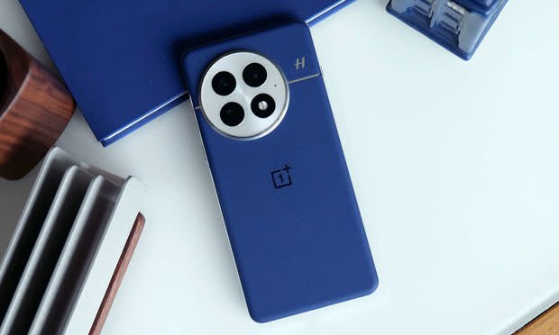 Imagen de la parte trasera de un OnePlus 13, en azul, en una mesa blanca.